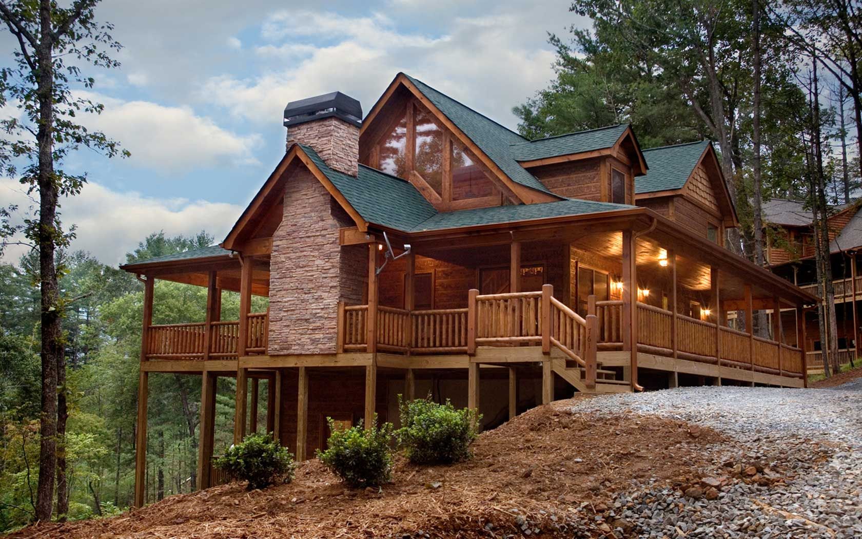 Reference lodge exterior with a wraparound veranda and evening arrival lighting